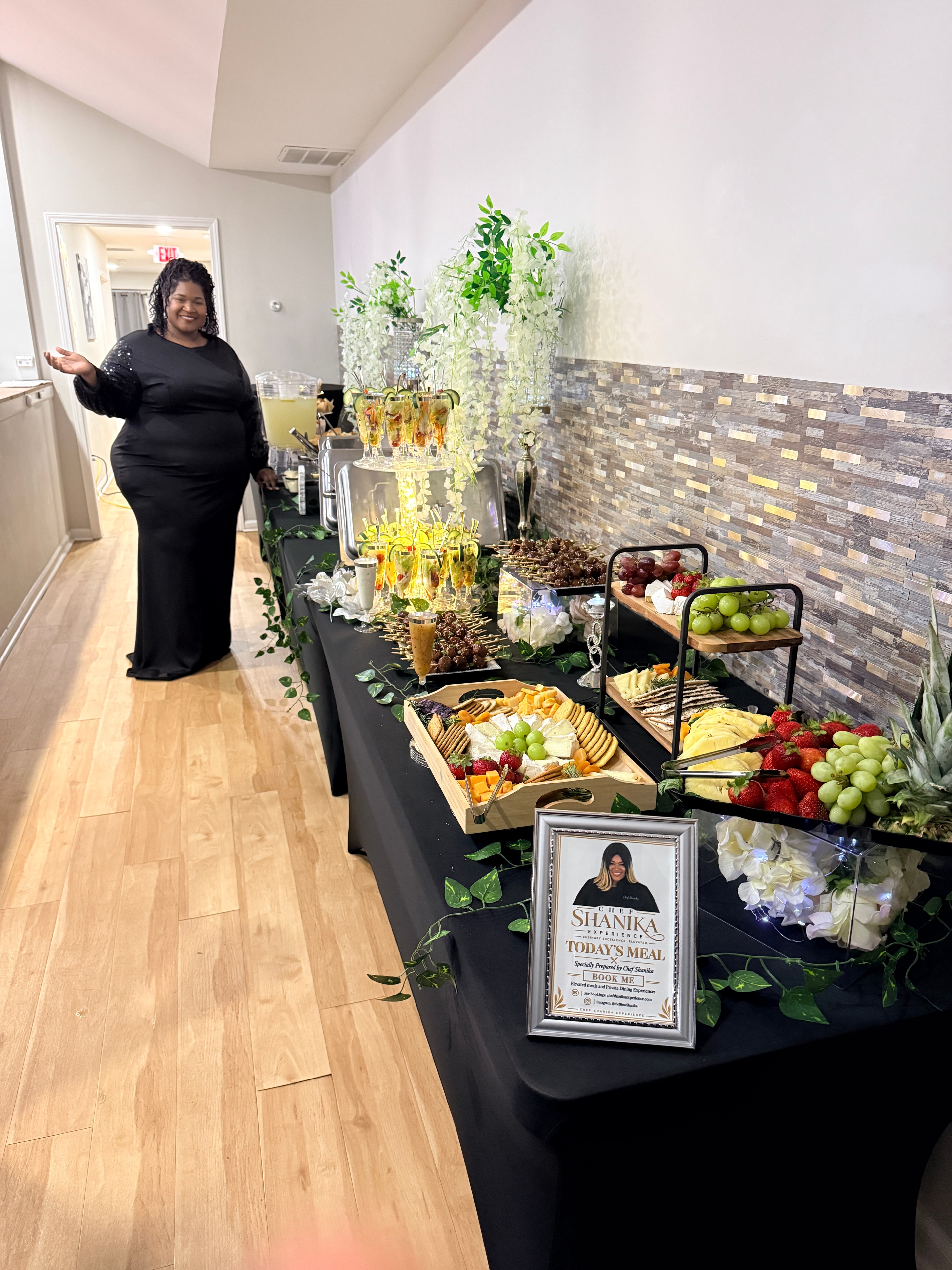 Chef Shanika beside a luxury event tablescape with fruit, charcuterie and floral arrangements